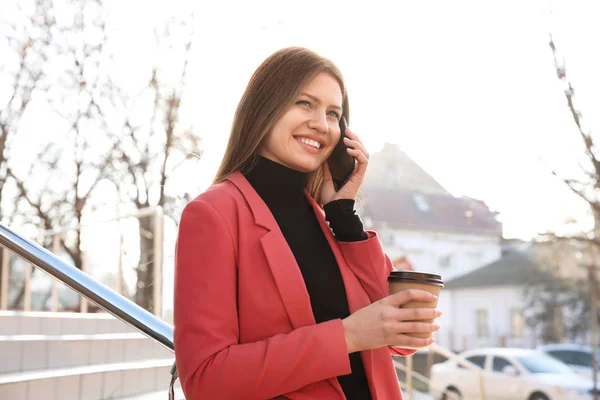 Mujer de negocios con taza de café hablando en smartphone en la ciudad s — Foto de Stock