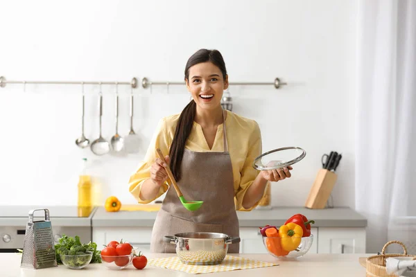 Giovane donna che cucina gustosa minestra in cucina — Foto Stock