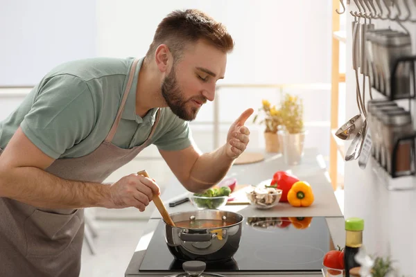 Młody człowiek gotowanie pyszne zupy w kuchni — Zdjęcie stockowe