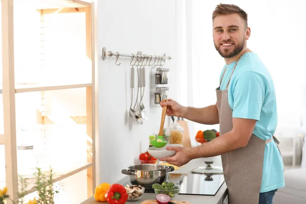 Young man pouring delicious soup into bowl at home