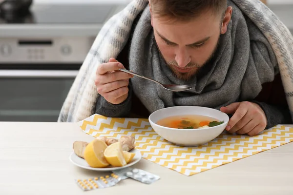 Jeune homme malade mangeant une soupe savoureuse pour guérir la grippe à table dans la cuisine — Photo