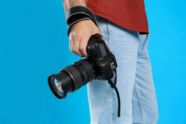 Professional photographer with modern camera on light blue backg