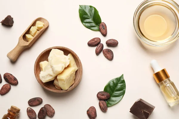 Organic cocoa butter, beans and essential oil on beige background, flat lay