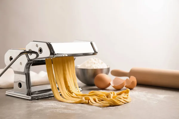 Pasta maker machine met deeg op grijze tafel. Ruimte voor tekst — Stockfoto