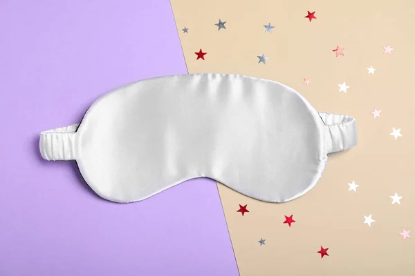White sleeping mask and glitter on color background, flat lay. Bedtime accessory