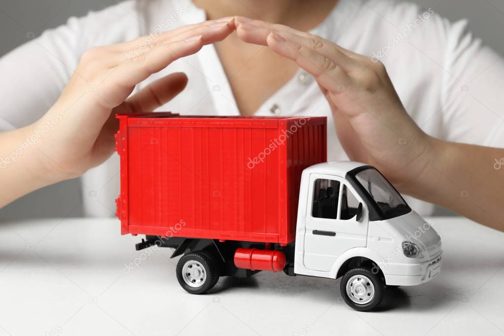 Woman covering toy truck at white table, closeup. Logistics and wholesale concept