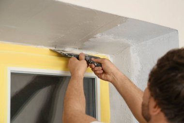 Pencere kenarına macun bıçağıyla sıva yapan bir adam, yakın plan. İç onarım