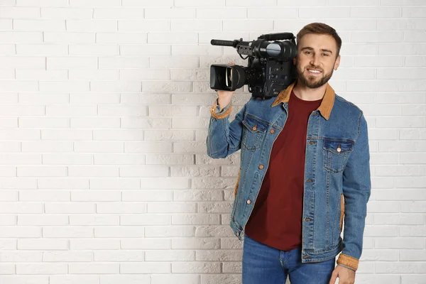 Operador con cámara de video profesional cerca de pared de ladrillo blanco, s — Foto de Stock