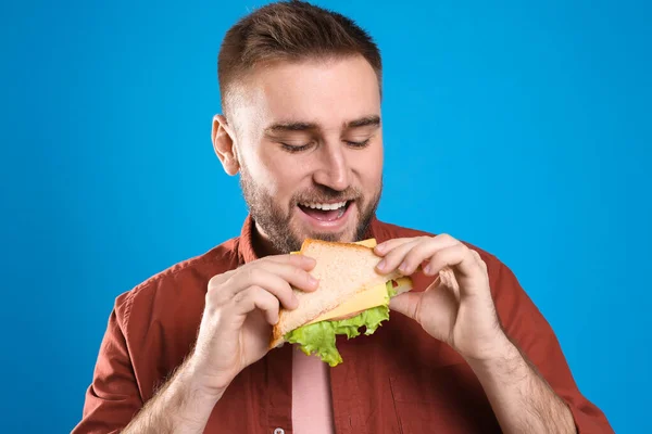 Young man eating tasty sandwich on light blue background — Stock Photo, Image