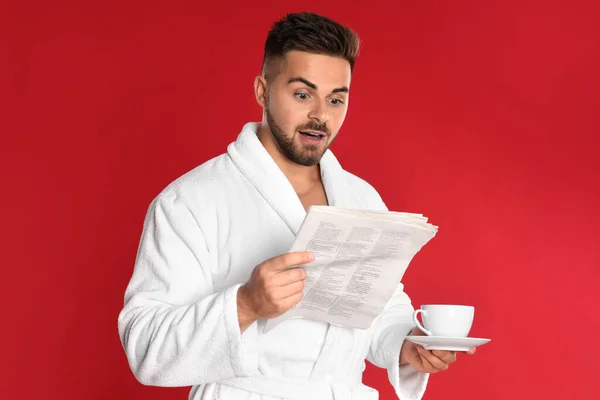 Bornozlu Genç Adam Elinde Kahve Fincanıyla Kırmızı Arka Planda Gazete — Stok fotoğraf