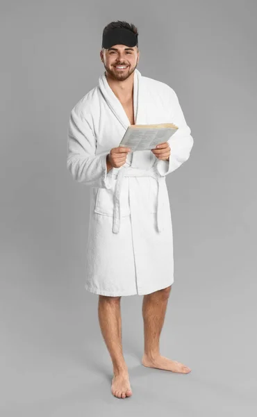 Young man in bathrobe reading newspaper on grey background — 스톡 사진