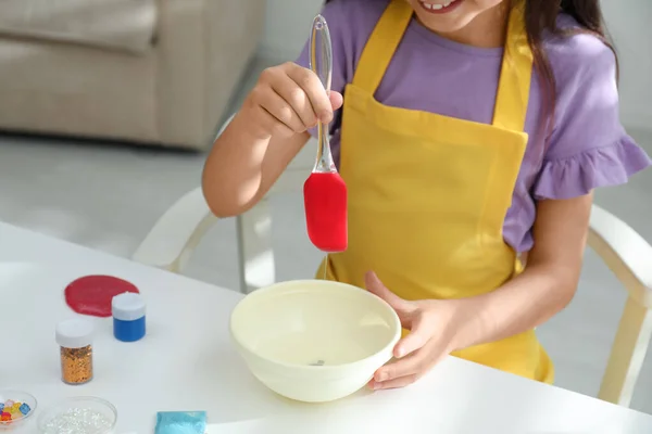 Маленькая девочка смешивает ингредиенты с силиконовой лопаткой за столом в — стоковое фото
