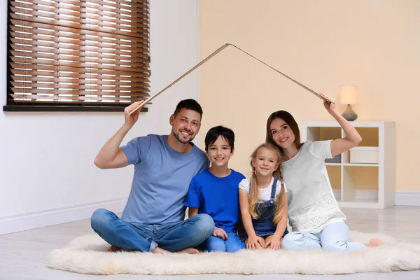 Família feliz sentada sob teto de papelão em casa. Condição de seguro — Fotografia de Stock
