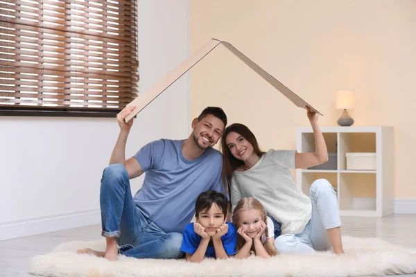 Happy family sitting under cardboard roof at home. Insurance con