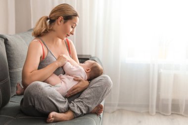 Genç bir kadın bebeğini evde emziriyor. Metin için boşluk