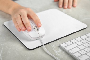 Woman using wired computer mouse on pad at light grey marble table, closeup clipart