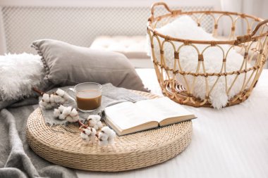 İçerideki hasır pouf hakkında bir bardak içki, pamuk ve kitapla kompozisyon