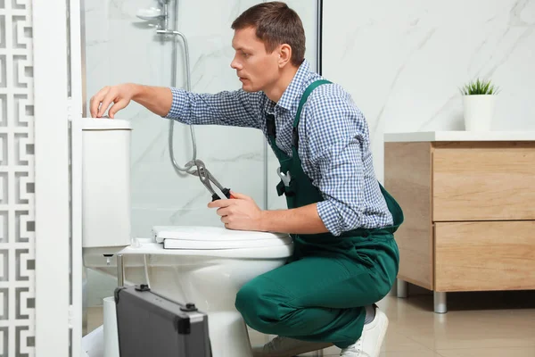 Encanador profissional reparando tanque sanitário no banheiro — Fotografia de Stock