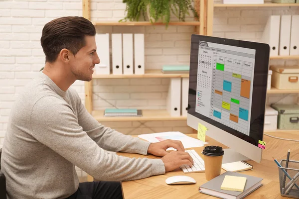 Hombre guapo utilizando la aplicación de calendario en el ordenador en la oficina —  Fotos de Stock