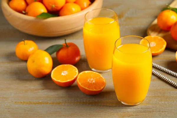 Стаканы свежего мандаринового сока и фрукты на деревянном столе — стоковое фото
