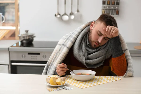 Jovem doente comendo sopa saborosa para curar a gripe à mesa na cozinha — Fotografia de Stock