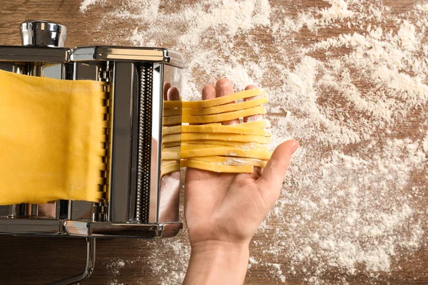 Mujer preparando fideos con máquina de hacer pasta en la mesa de madera — Foto de Stock