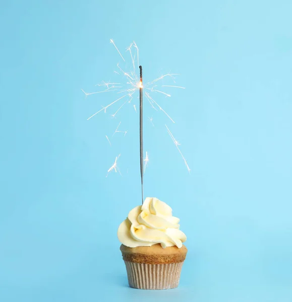 Birthday cupcake with sparkler on light blue background