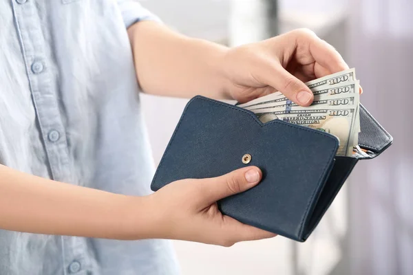 Mujer poniendo dinero en la cartera sobre fondo borroso, primer plano —  Fotos de Stock