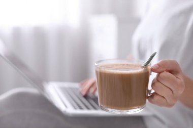 Sabah kahvesi içen kadın laptopla içeride çalışıyor, yakın plan. Metin için boşluk