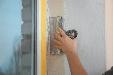 Pencere kenarına macun bıçağıyla sıva yapan bir adam, yakın plan. İç onarım