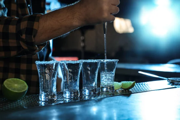 Bartender pouring Mexican Tequila into shot glasses at bar counter, closeup