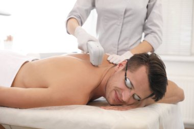 Young man undergoing laser epilation procedure in beauty salon clipart