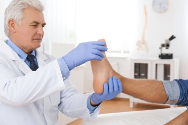 Erkek ortopedist klinikte hastanın ayağını kontrol ediyor.