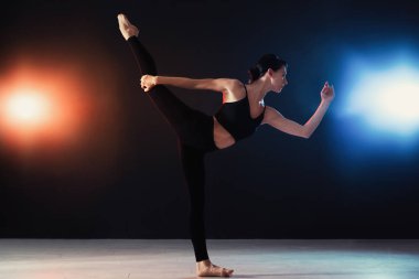 Genç profesyonel akrobat karanlık stüdyoda egzersiz yapıyor.