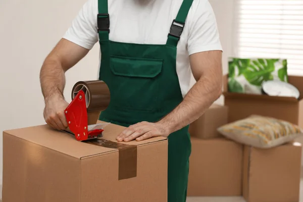 Man packing box with adhesive tape indoors, closeup. Moving serv — Stock Photo, Image