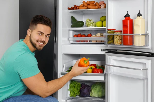 Jeune homme sortant le poivron du réfrigérateur intérieur — Photo