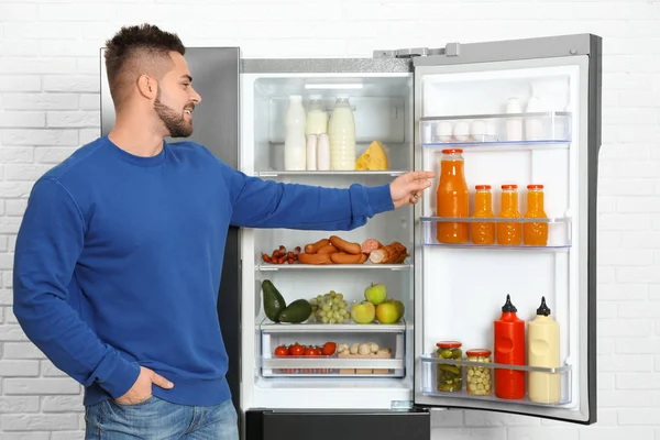 Молодой человек берет сок из холодильника в помещении — стоковое фото