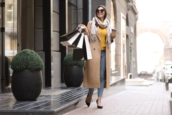 Mulher bonita com xícara de café e sacos de compras em ci — Fotografia de Stock
