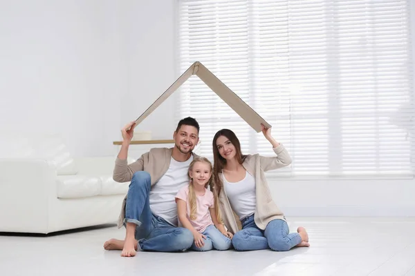 Feliz familia sentada bajo el techo de cartón en casa. Seguro con —  Fotos de Stock