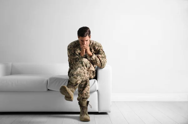 Stressed military officer sitting on sofa near white wall indoor — ストック写真