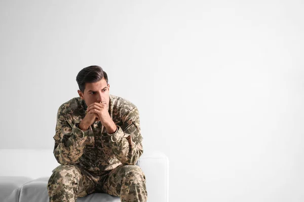 Stressed military officer sitting on sofa against white backgrou