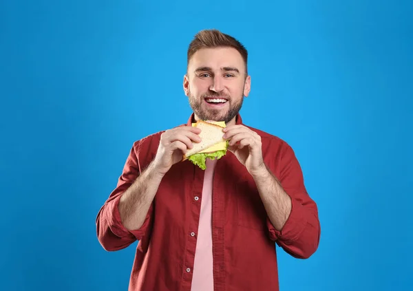 Young man with tasty sandwich on light blue background — Stock Photo, Image