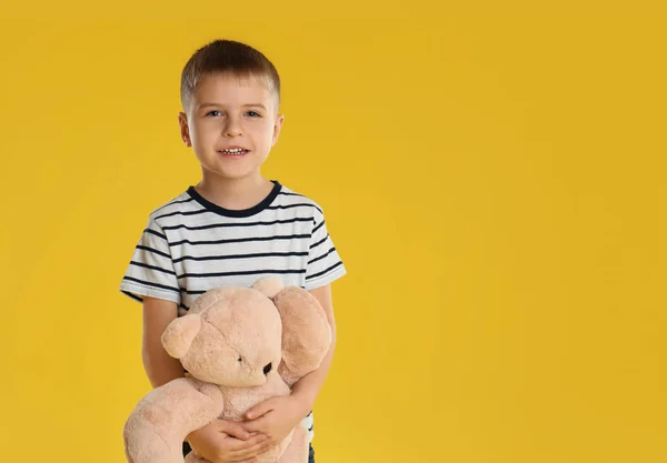 Kleine jongen met speelgoedbeer op gele achtergrond. Ruimte voor tekst — Stockfoto
