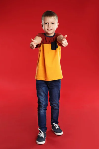 Kisfiú mutatja hüvelykujját fel a piros háttér — Stock Fotó