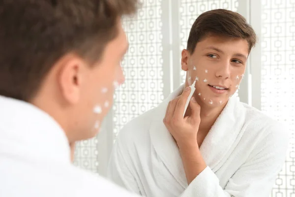 Teen guy with acne problem applying cream near mirror in bathroo — ストック写真