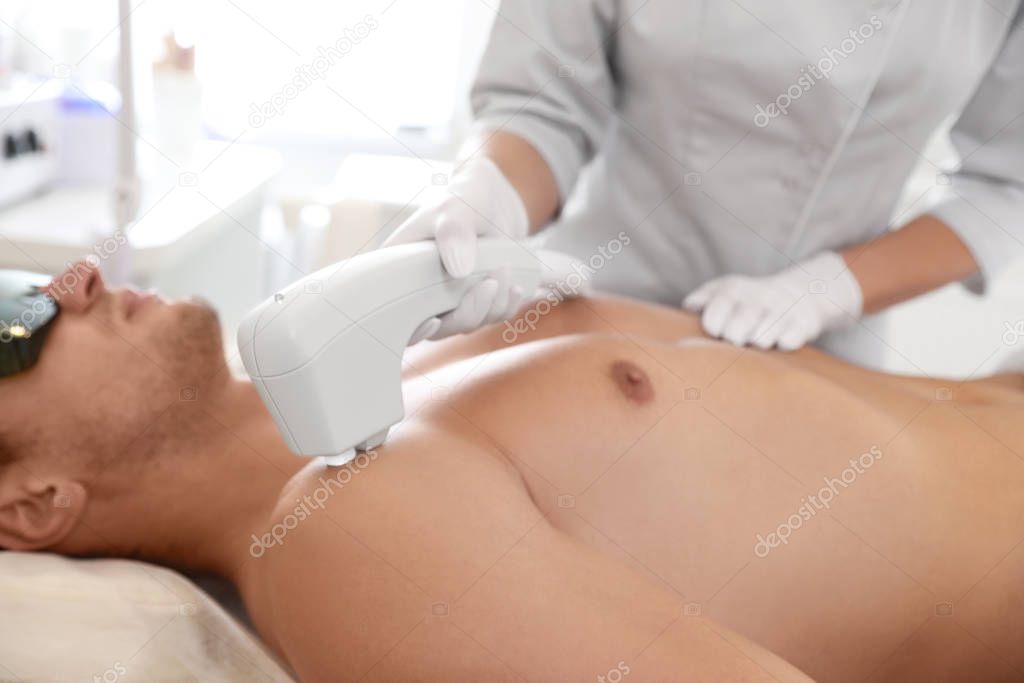 Young man undergoing laser epilation procedure in beauty salon, 