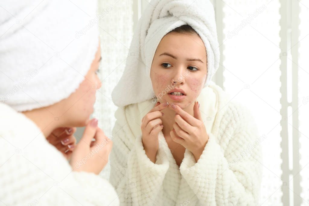 Teen girl with acne problem squeezing pimple near mirror in bath