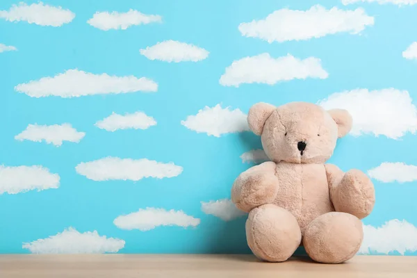 Teddy bear on wooden table near wall with painted blue sky, spac — Stock Photo, Image