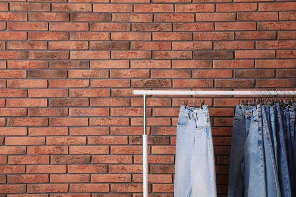 Rack with stylish jeans near brick wall. Space for text — Stock Photo, Image