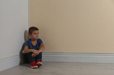 Küçük çocuk sarı duvarın yanında köşede oturuyor, mesaj için yer var. Çocuk tehlikede.
